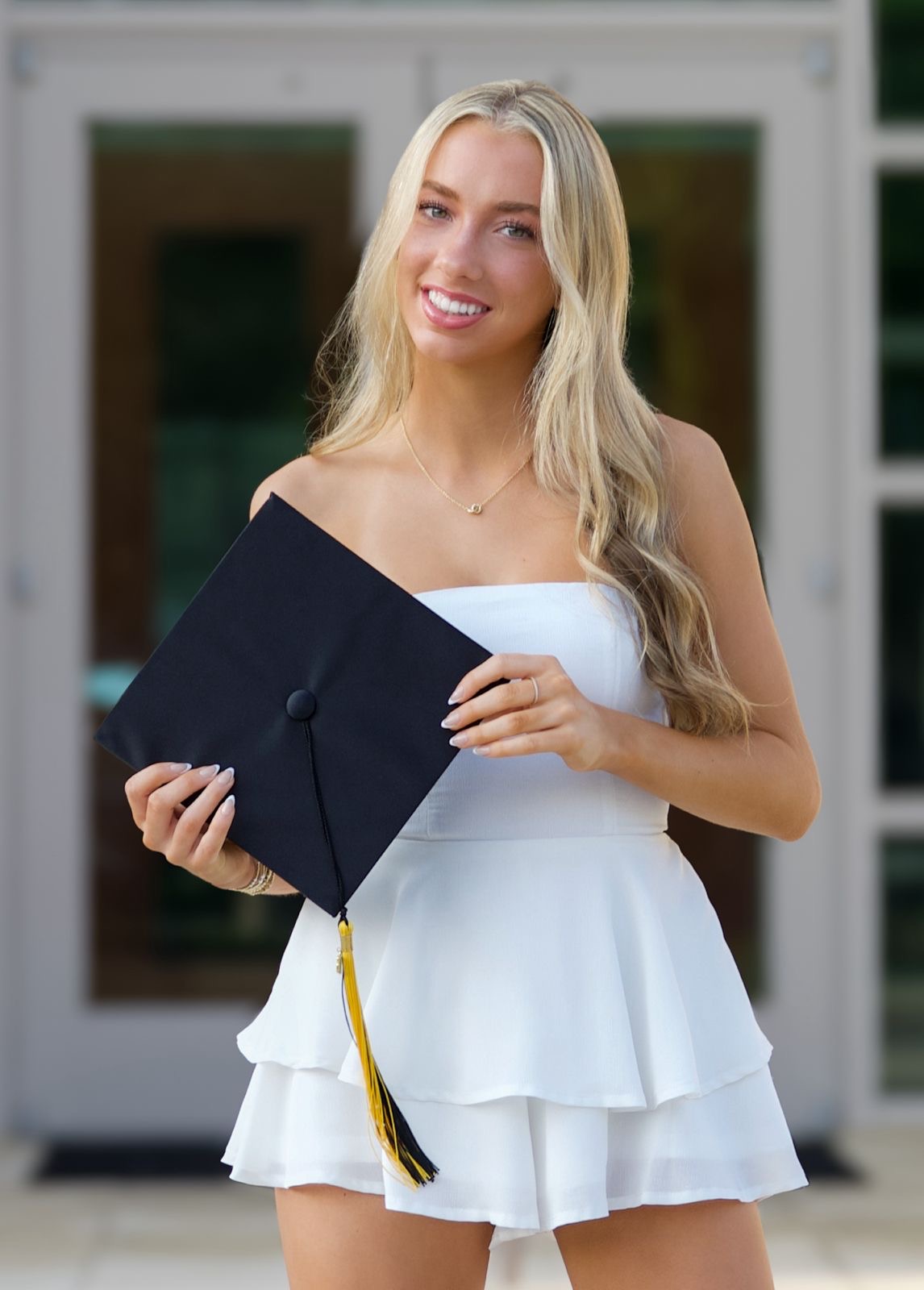 Graduate in a white dress holding a black graduation cap
